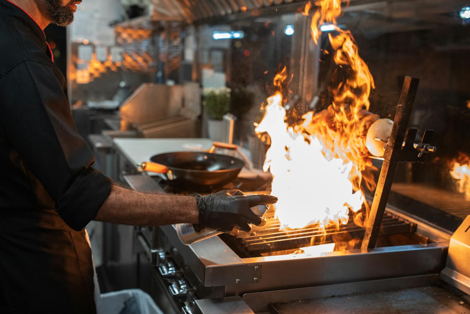 Chef at a wood-fired grill, flame rising over the grate during service.