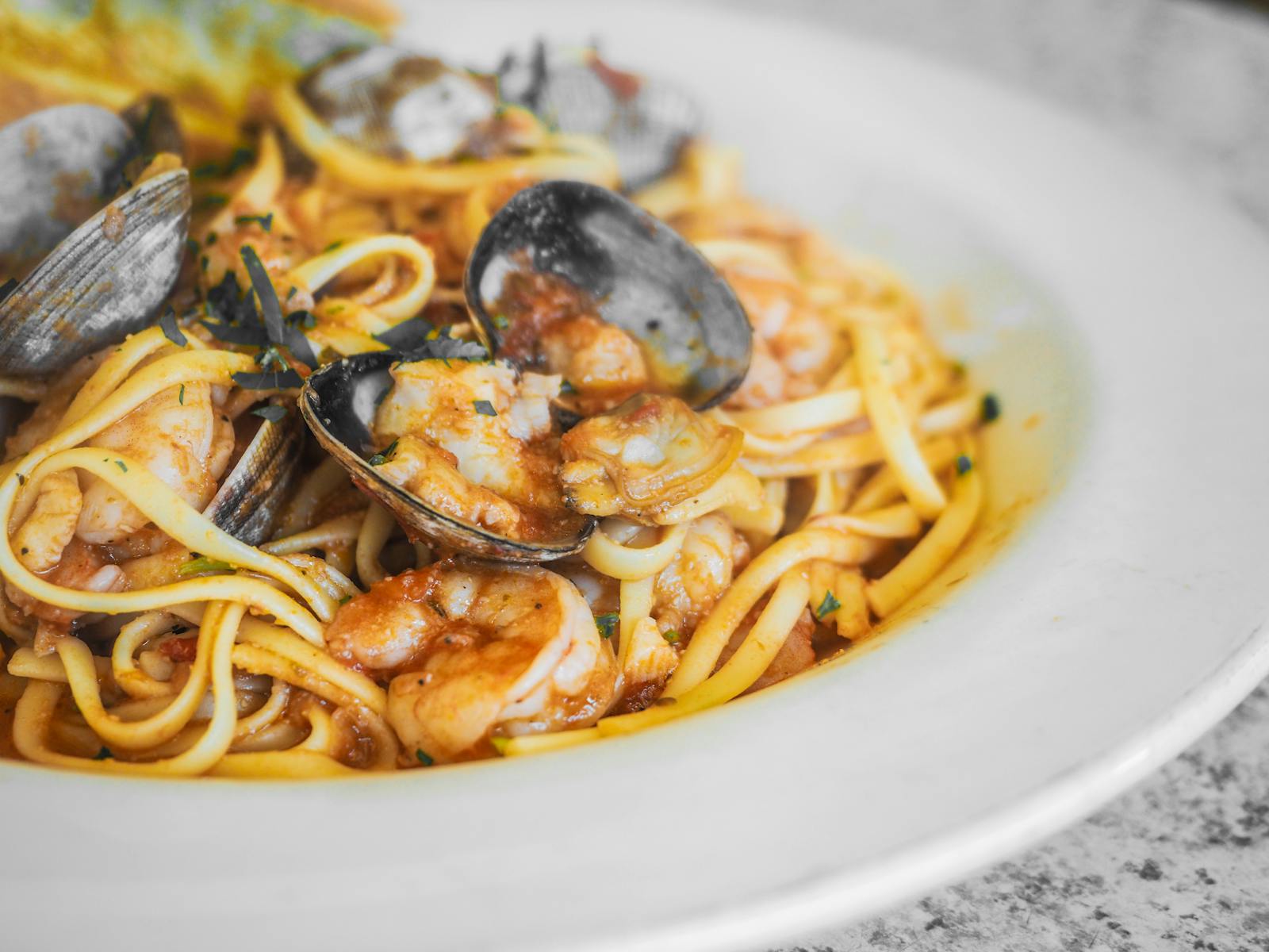 Ribbon pasta tossed with mussels, shrimp, and a light tomato sauce, parsley on top.