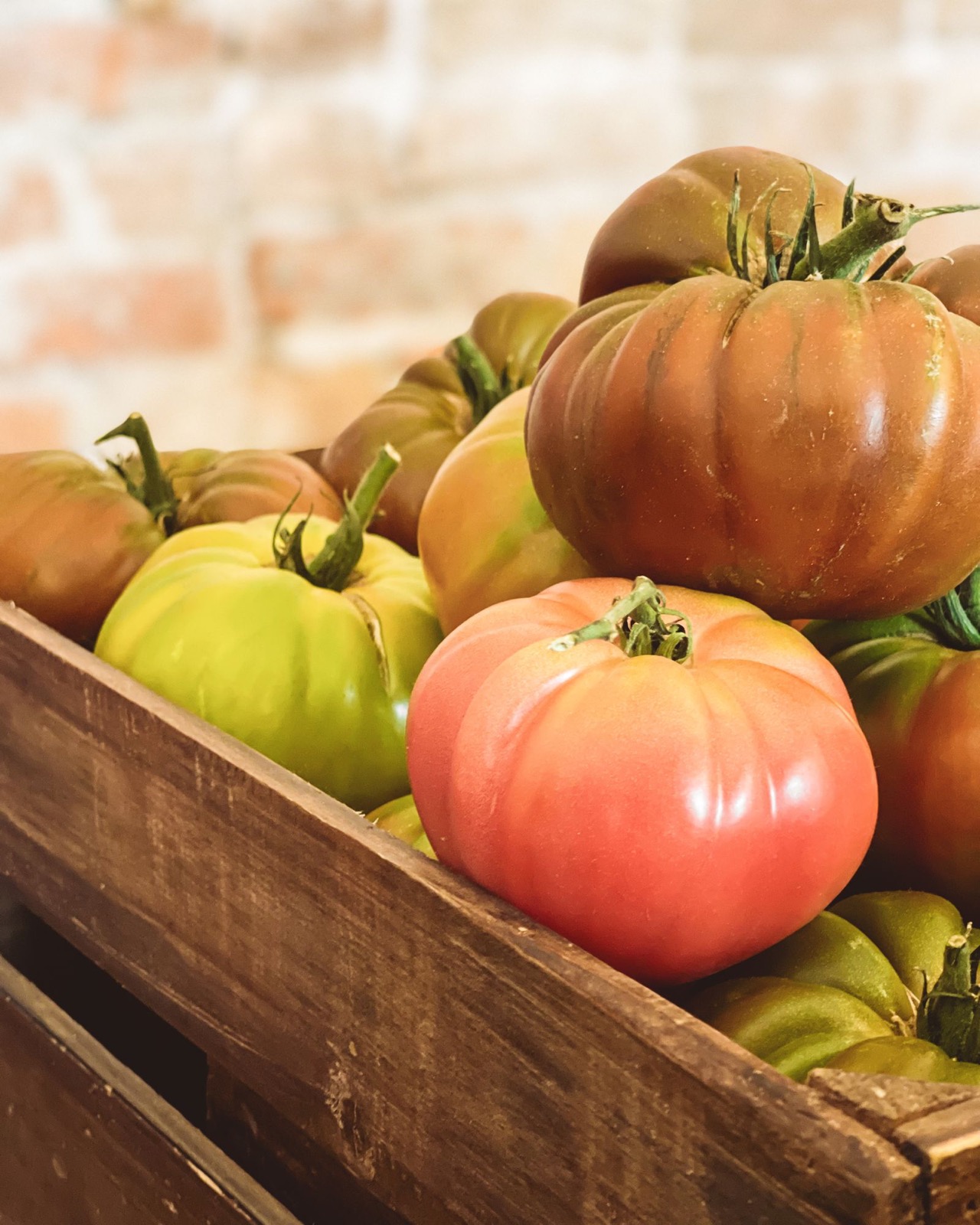 Multicolor heirloom tomatoes piled in a rustic wooden crate.